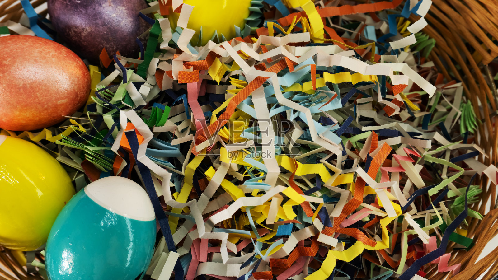 彩色的复活节彩蛋用不同颜色的纸装饰，放在篮子里。照片摄影图片
