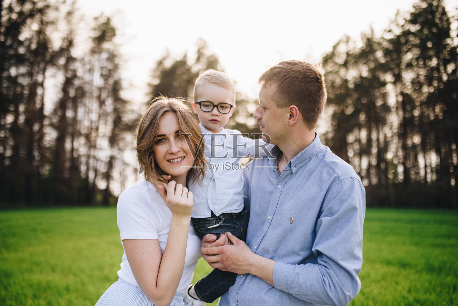 家庭在自然界中。在森林里，在草地上野餐。绿色的草。蓝色的衣服。妈妈，爸爸，戴眼镜的儿子。金发男孩。欢乐。父母与孩子玩耍。在一起。野餐篮子。食物、毛毯照片摄影图片