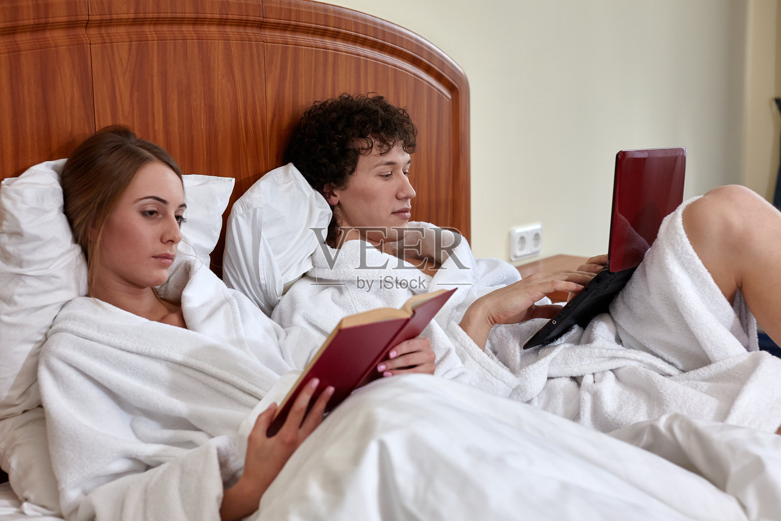 有笔记本电脑和书的家人躺在家里的床上。周末或独处，保持社交距离。远程学习与工作照片摄影图片