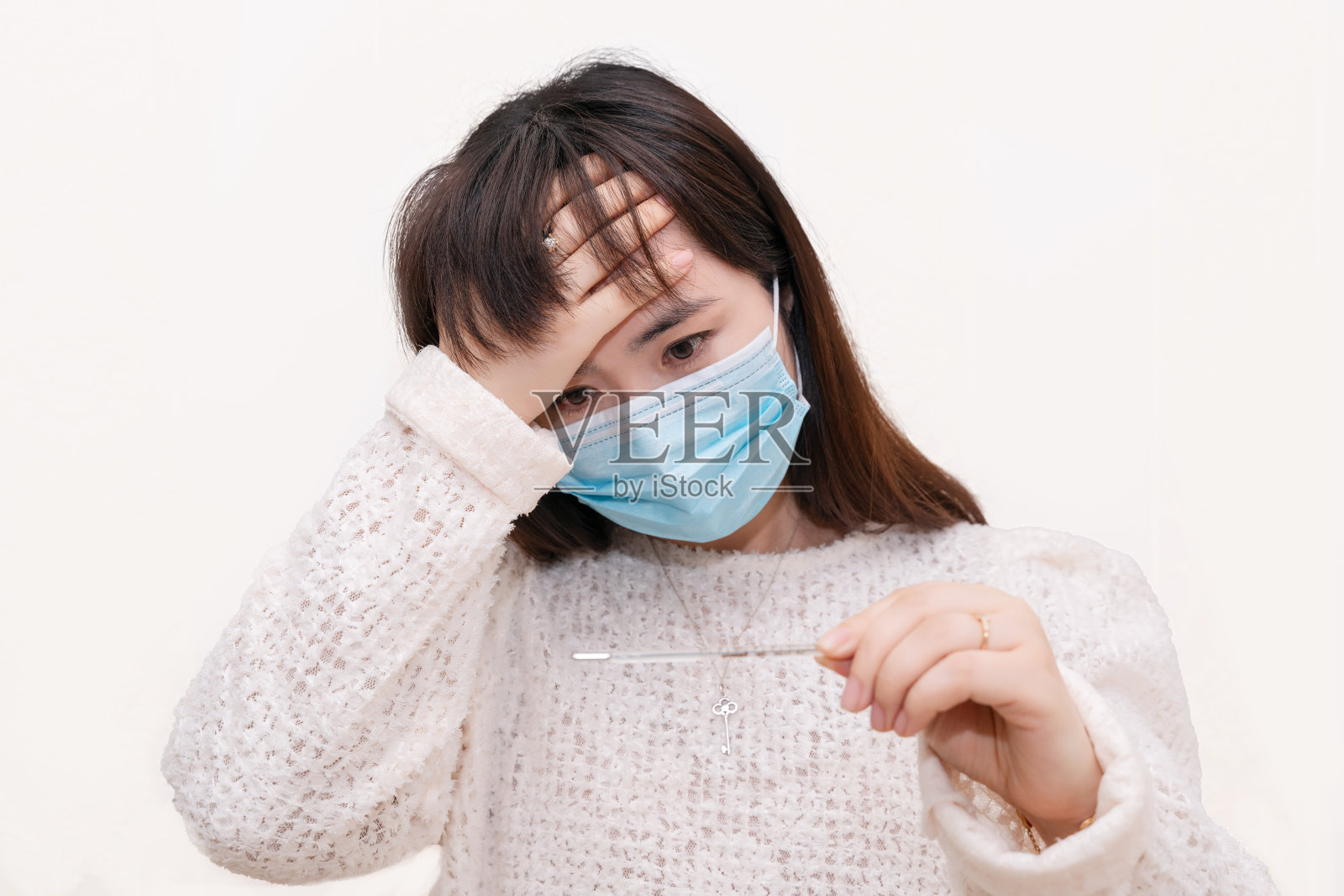 一个亚洲妇女戴着口罩，触摸她的额头，感觉温度和看温度计照片摄影图片