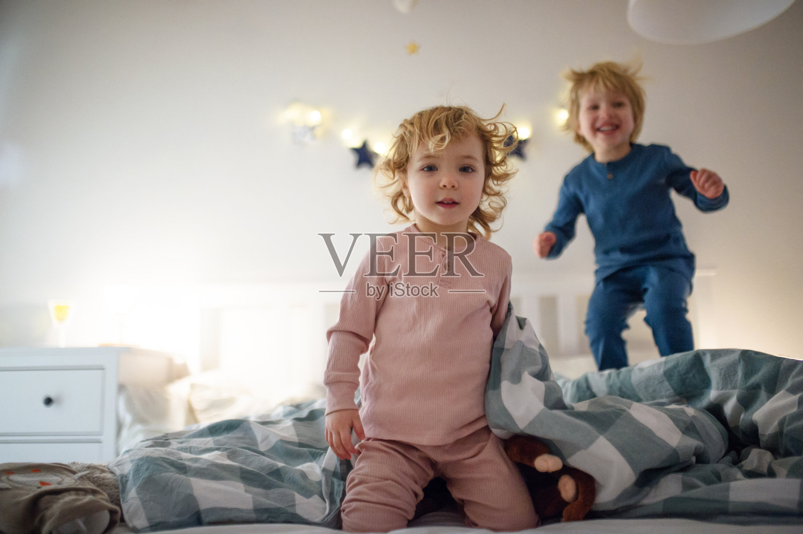 两个小孩子在家里的床上蹦蹦跳跳，玩得很开心。照片摄影图片