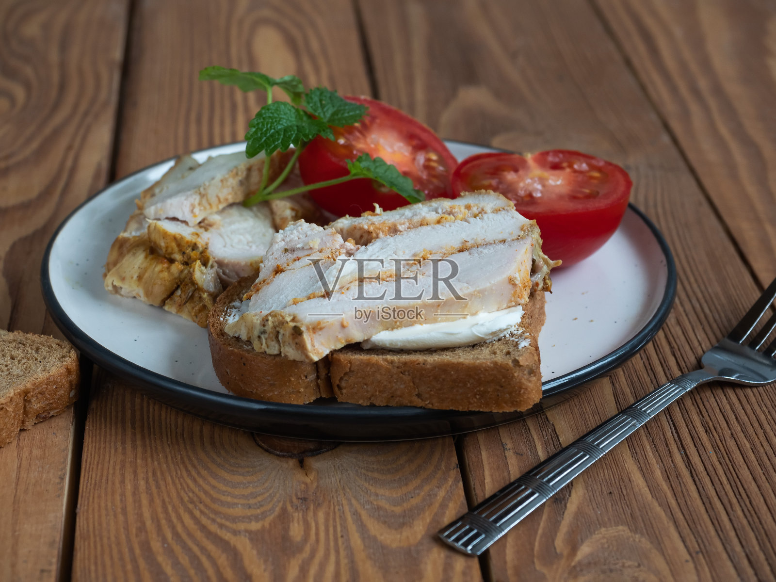 木桌上的陶瓷盘子上放着鸡肉、火腿和番茄三明治照片摄影图片