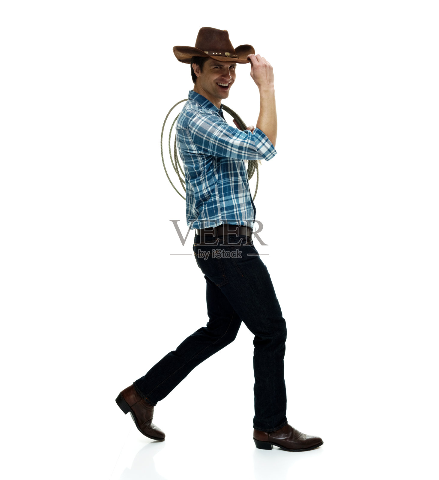 白人年轻男性牛仔戴着帽子，手持套索，用绳子在白色背景前行走照片摄影图片