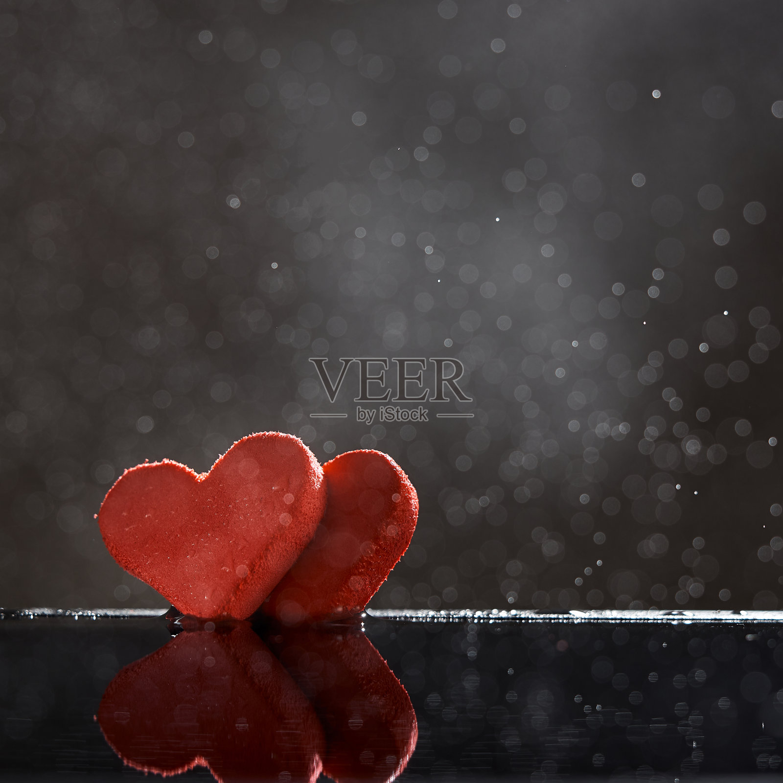 两颗红色的心与雨滴倒映在水中，以一个散景的黑色背景。有拷贝空间的照片。照片摄影图片