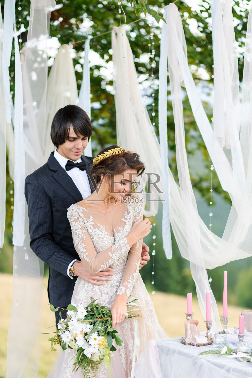 新娘和新郎在一棵老橡树下拥抱在一起。在山上拍摄婚纱照。旁边是为仪式准备的装饰。照片摄影图片