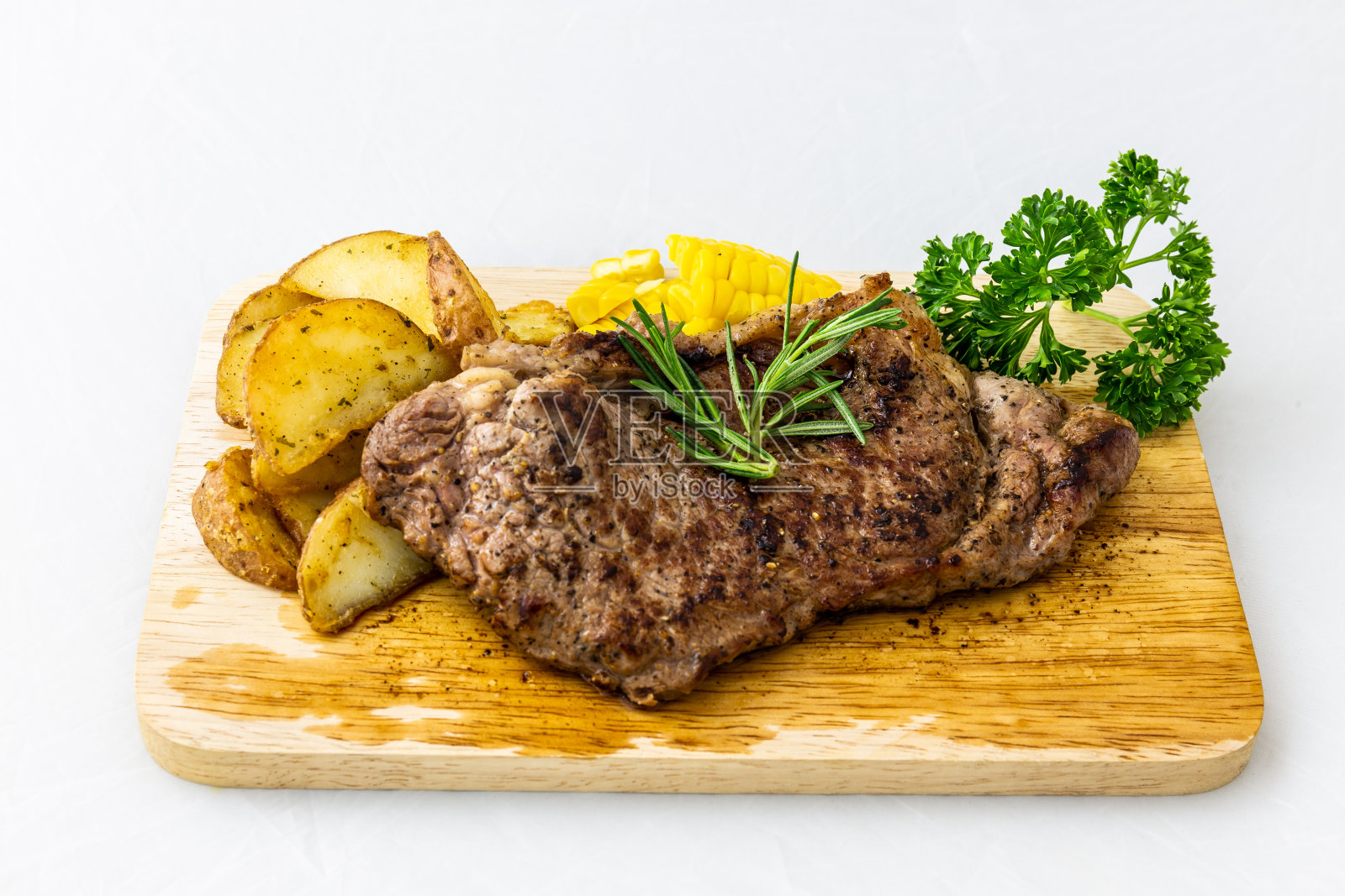 木托盘上的牛排，土豆，欧芹，迷迭香，玉米，白色背景照片摄影图片