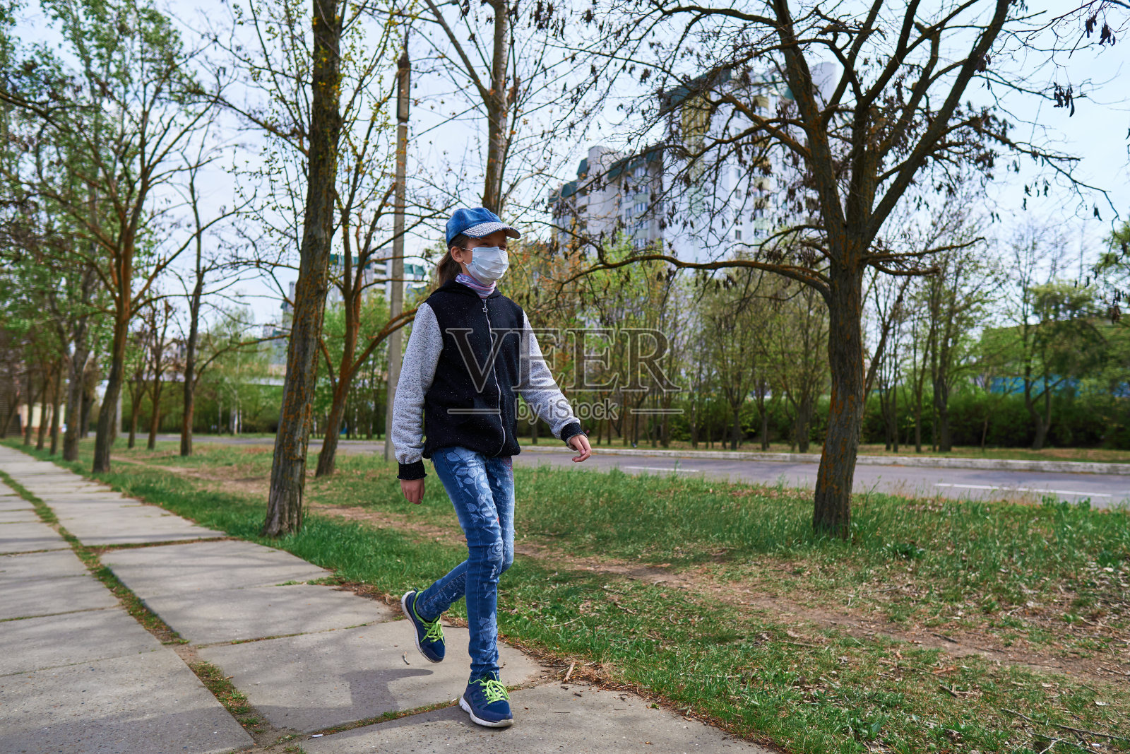 一个小女孩白天走在街道上，有人行道，有高楼大厦，有居民区，她脸上戴着医用口罩，防止病毒和灰尘照片摄影图片