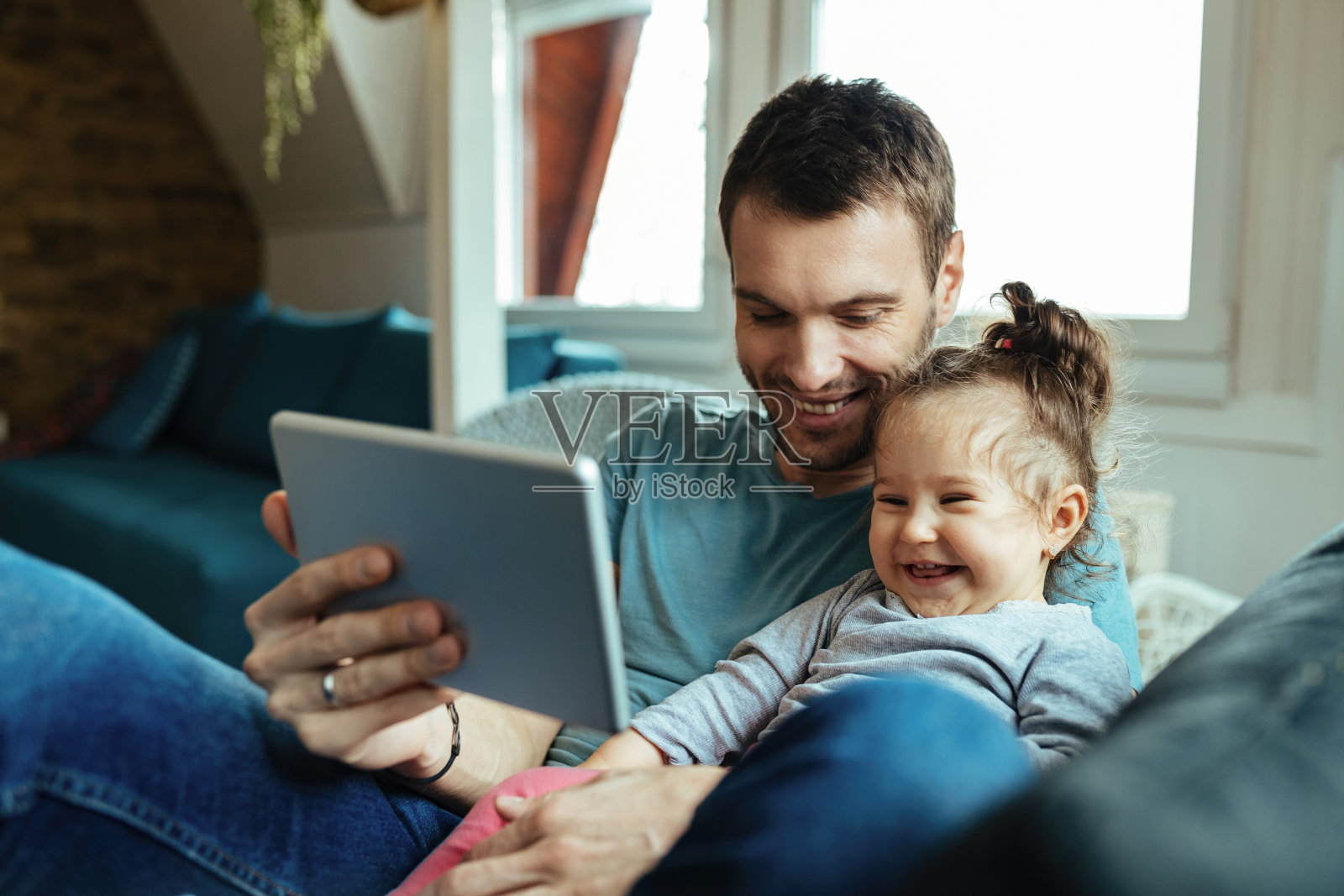 快乐的父亲和小女儿在家里使用触摸板玩得开心。照片摄影图片
