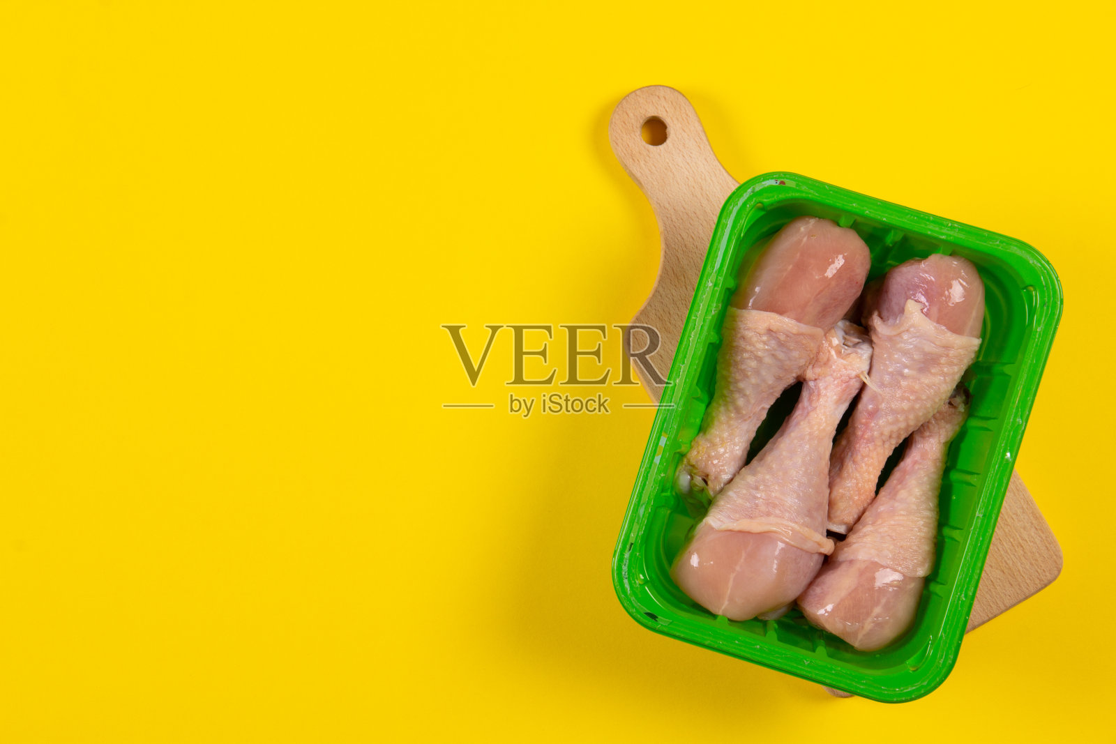 黄色背景的塑料容器里的冻鸡腿照片摄影图片
