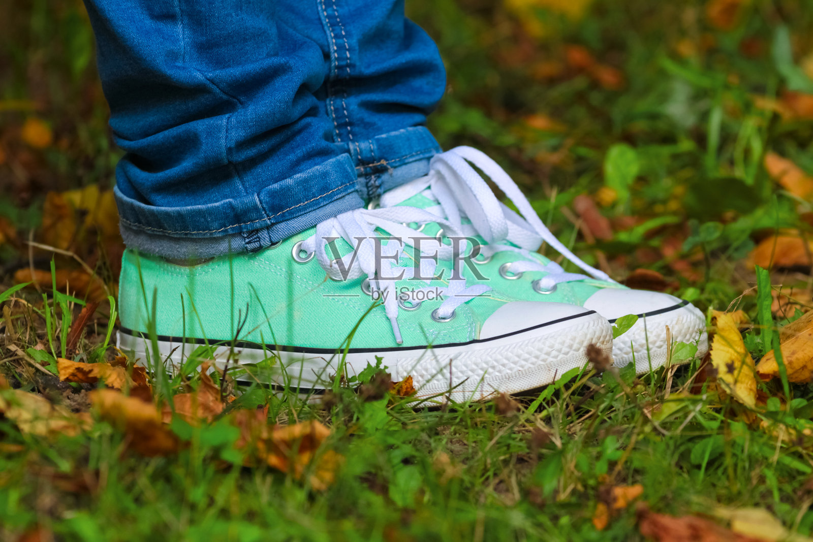 穿着蓝色牛仔裤和运动鞋的脚踩在秋天的落叶草地上照片摄影图片