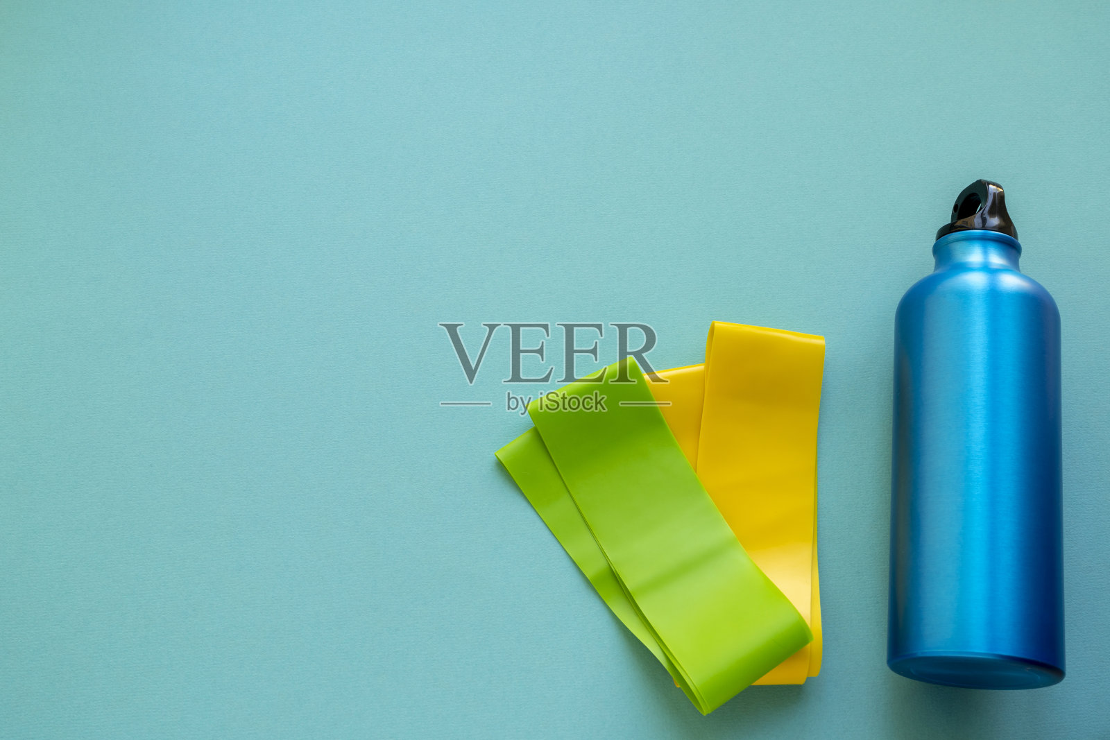 蓝色背景上的一瓶水和健身橡皮筋。运动的趋势。健康的概念照片摄影图片