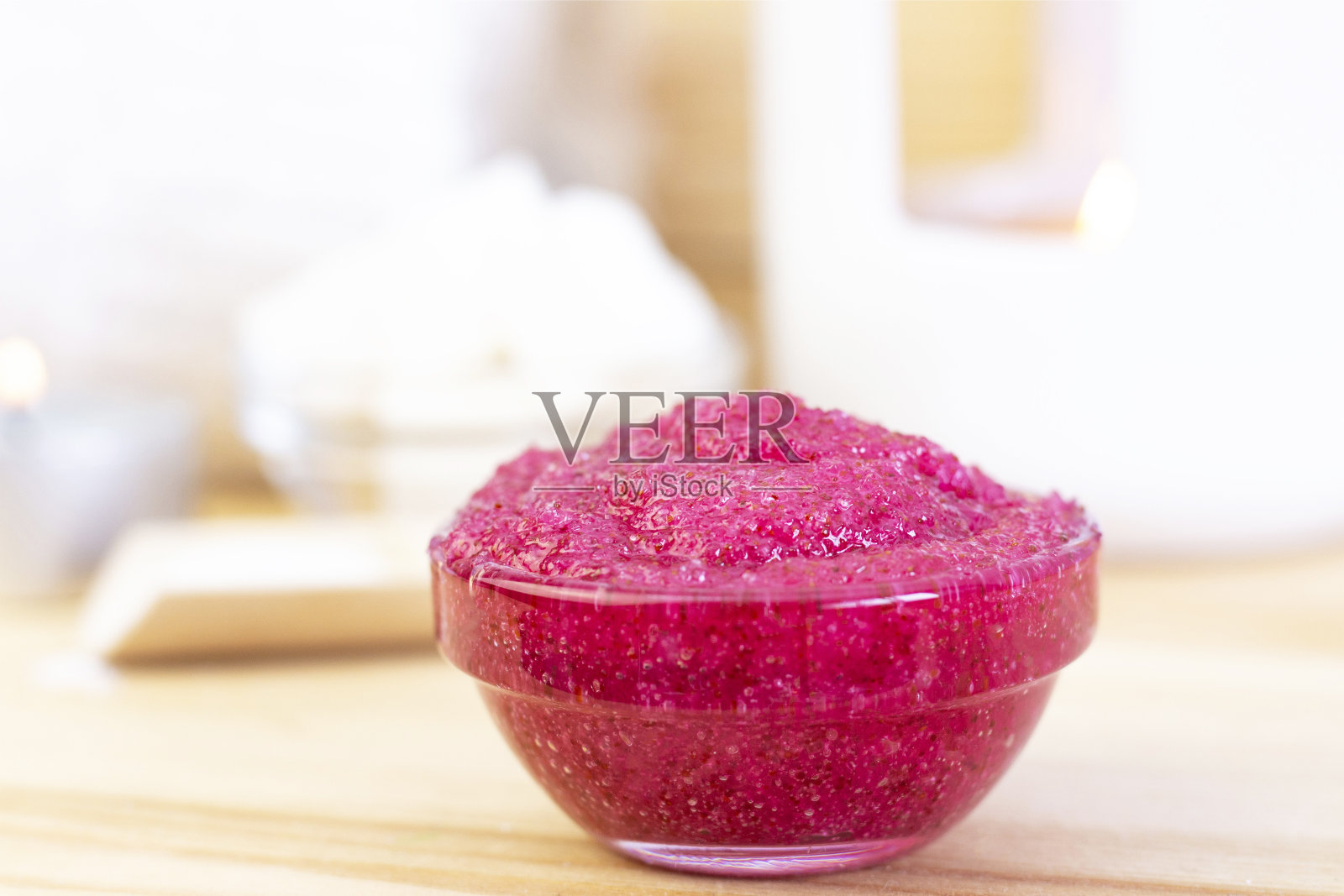 用糖制成的天然粉色身体磨砂膏。用玻璃杯装上粉色的磨砂膏，背景是蜡烛和糖。照片摄影图片