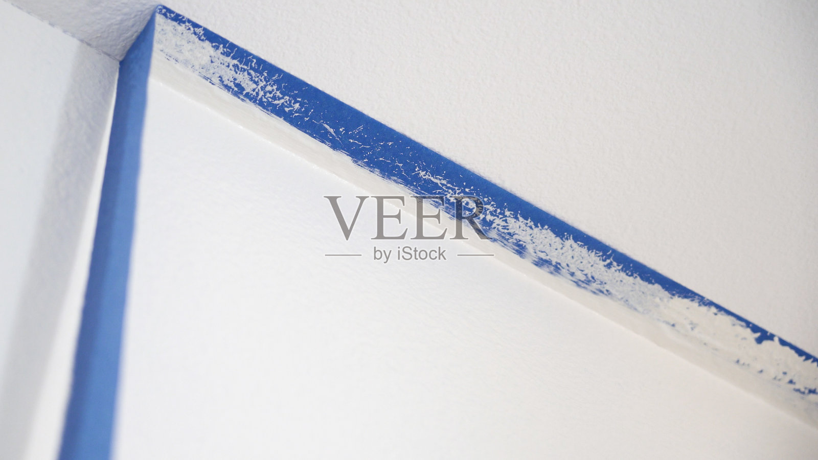 从天花板上拆除遮蔽胶带。一个油漆工从墙上扯下蓝色的油漆工胶带，露出天花板的干净边缘。照片摄影图片