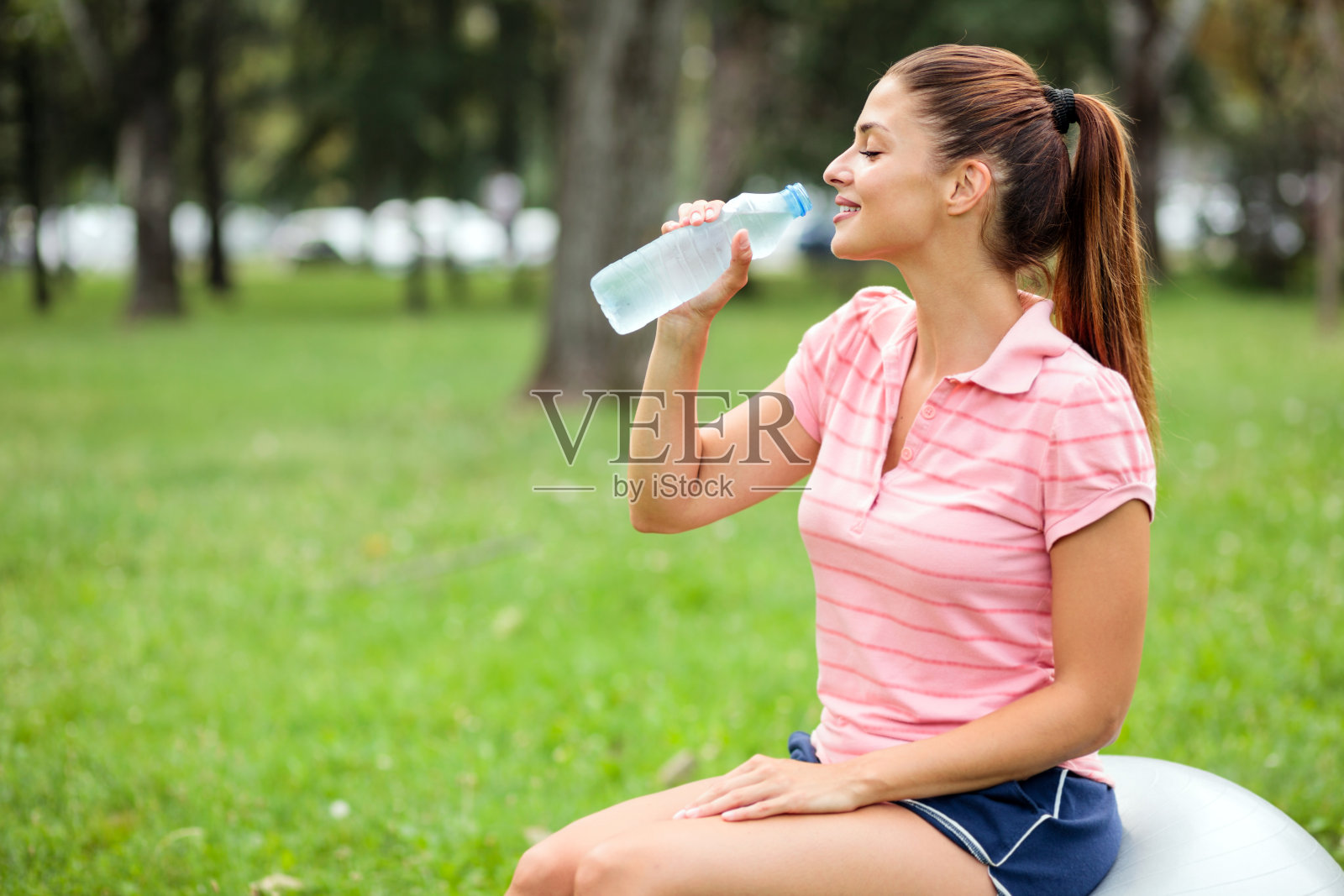 年轻女子在公园剧烈运动后，喝着水放松照片摄影图片