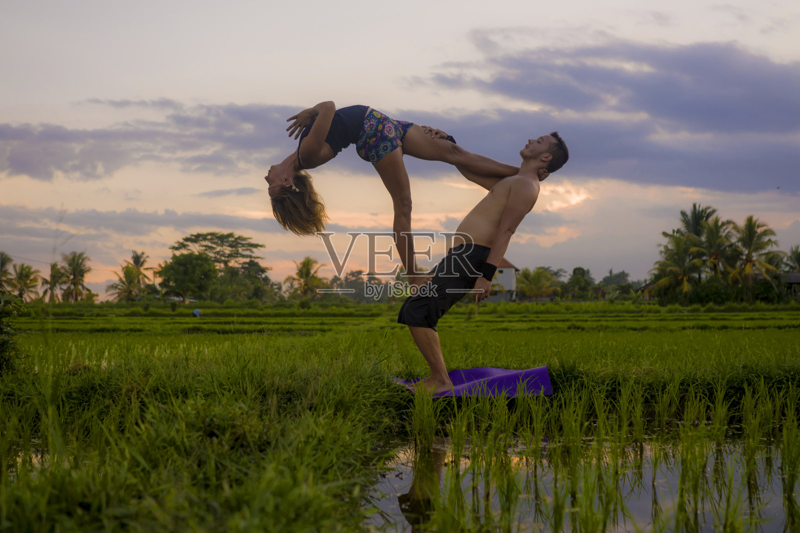 户外日落acroyoga锻炼剪影-年轻快乐和适合夫妇练习跨越瑜伽练习在美丽的稻田享受自然和健康的生活方式做杂技姿势照片摄影图片