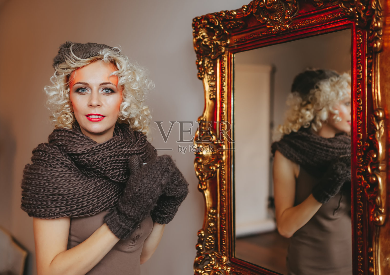 年轻的金发卷毛的女人看着镜头，站在大镜子旁边照片摄影图片