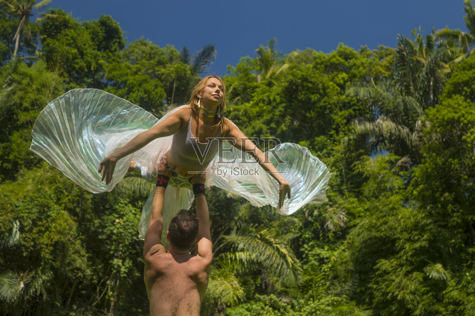 瑜伽健身——一对年轻迷人的幸福情侣在热带的绿色森林里做acroyoga，享受大自然，女孩展翅飞翔，由男人在健康的生活方式和健身照片摄影图片