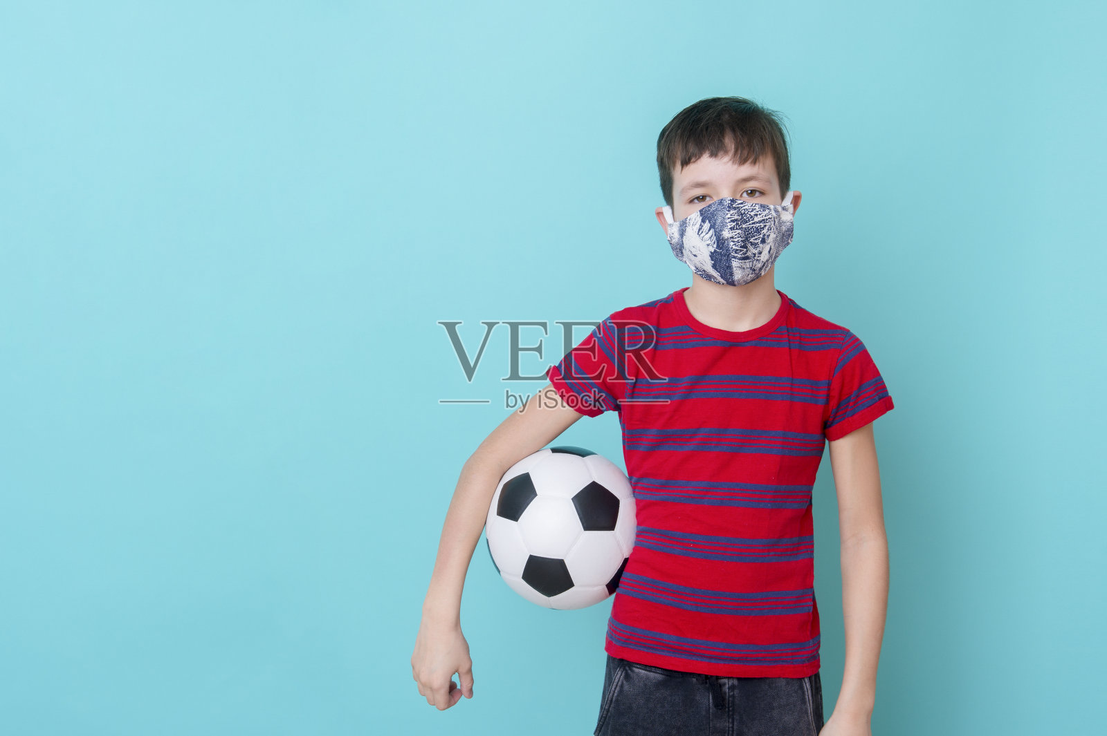 因为冠状病毒戴面具的男孩在蓝色背景上玩球。训练网络的概念。照片摄影图片