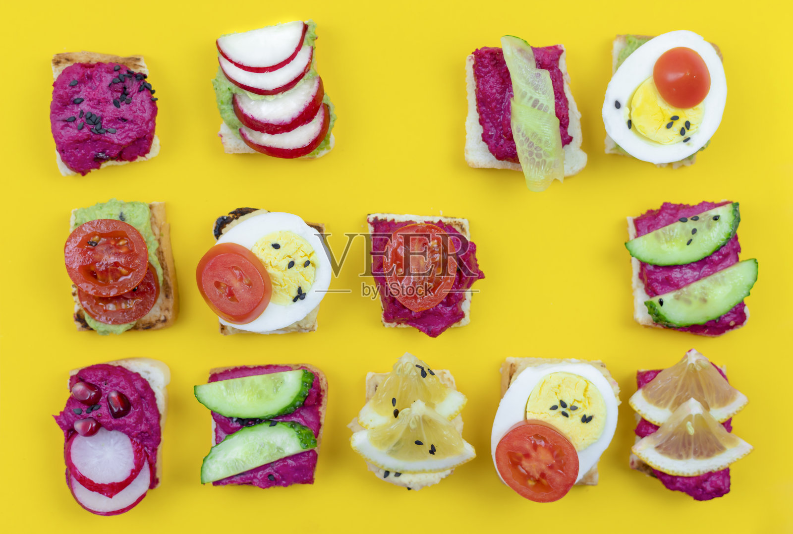 不同的烤面包三明治配甜菜鹰嘴豆泥，鳄梨色拉酱，不同的蔬菜。素食helsifood概念。夏天的零食。黄色背景上的食物图案照片摄影图片