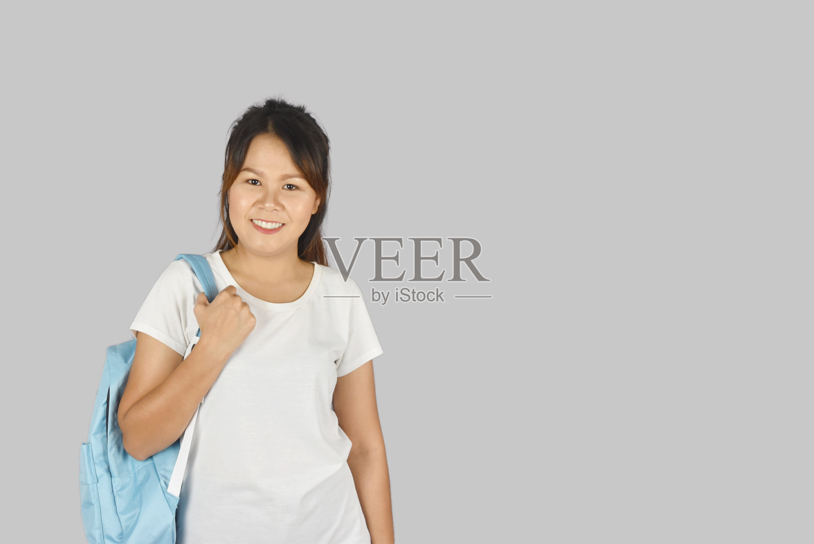 亚洲美丽的年轻学生微笑与背包在灰色的背景与拷贝的空间。照片摄影图片