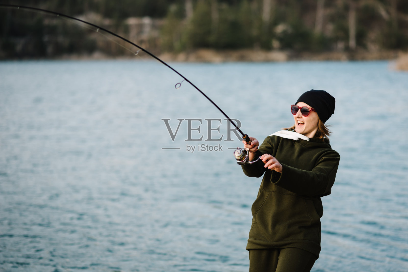 一个女人在抓鱼，一边拉钓竿一边钓鱼。女孩钓鱼码头上的湖或池塘与文本空间。渔夫拿着钓竿，在河岸上旋转卷轴。捕狗鱼、鲈鱼、鲤鱼。野生自然。照片摄影图片