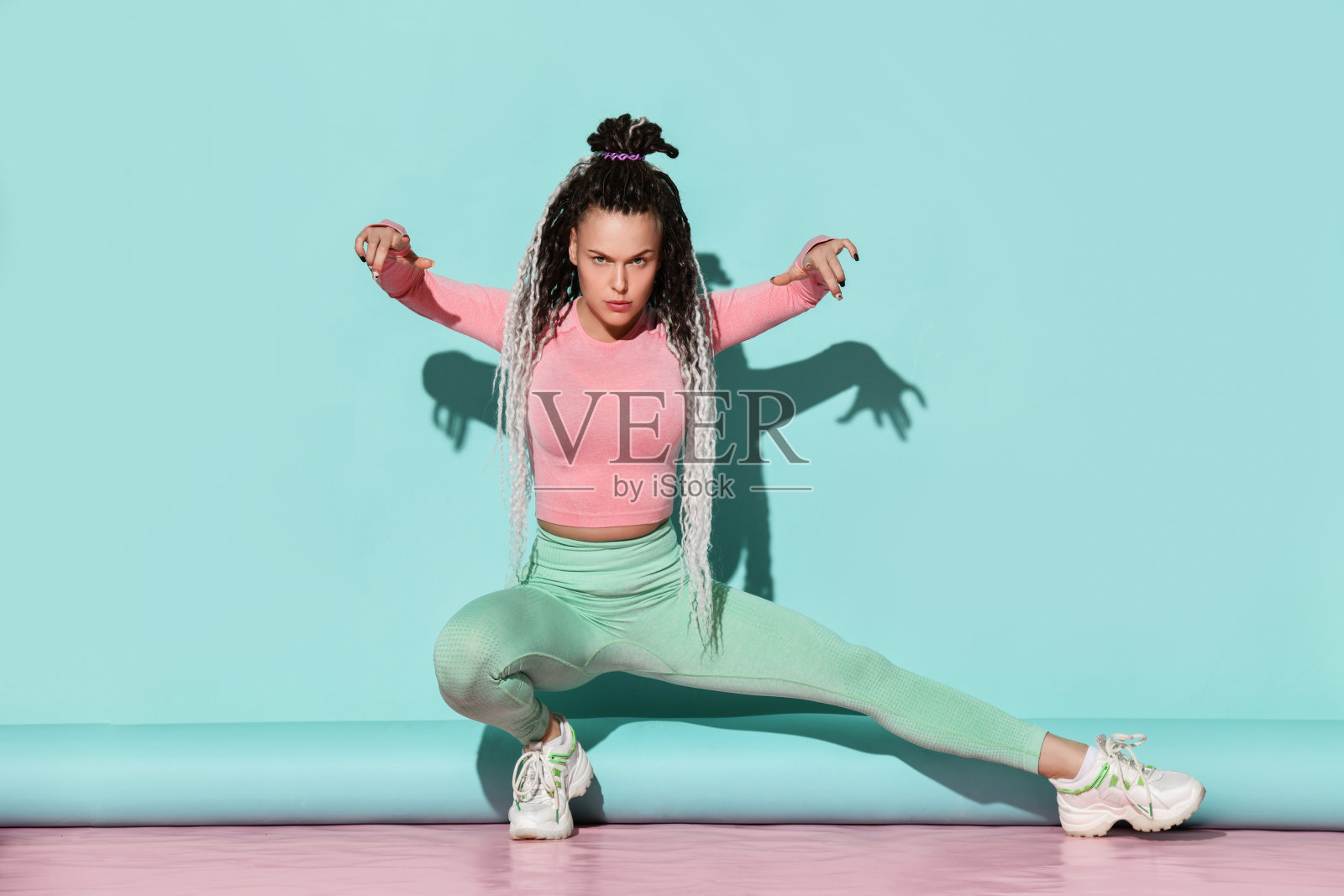 年轻美丽的微笑女孩，梳着发辫，穿着运动服和运动鞋坐在地板上，努力保持身体平衡照片摄影图片