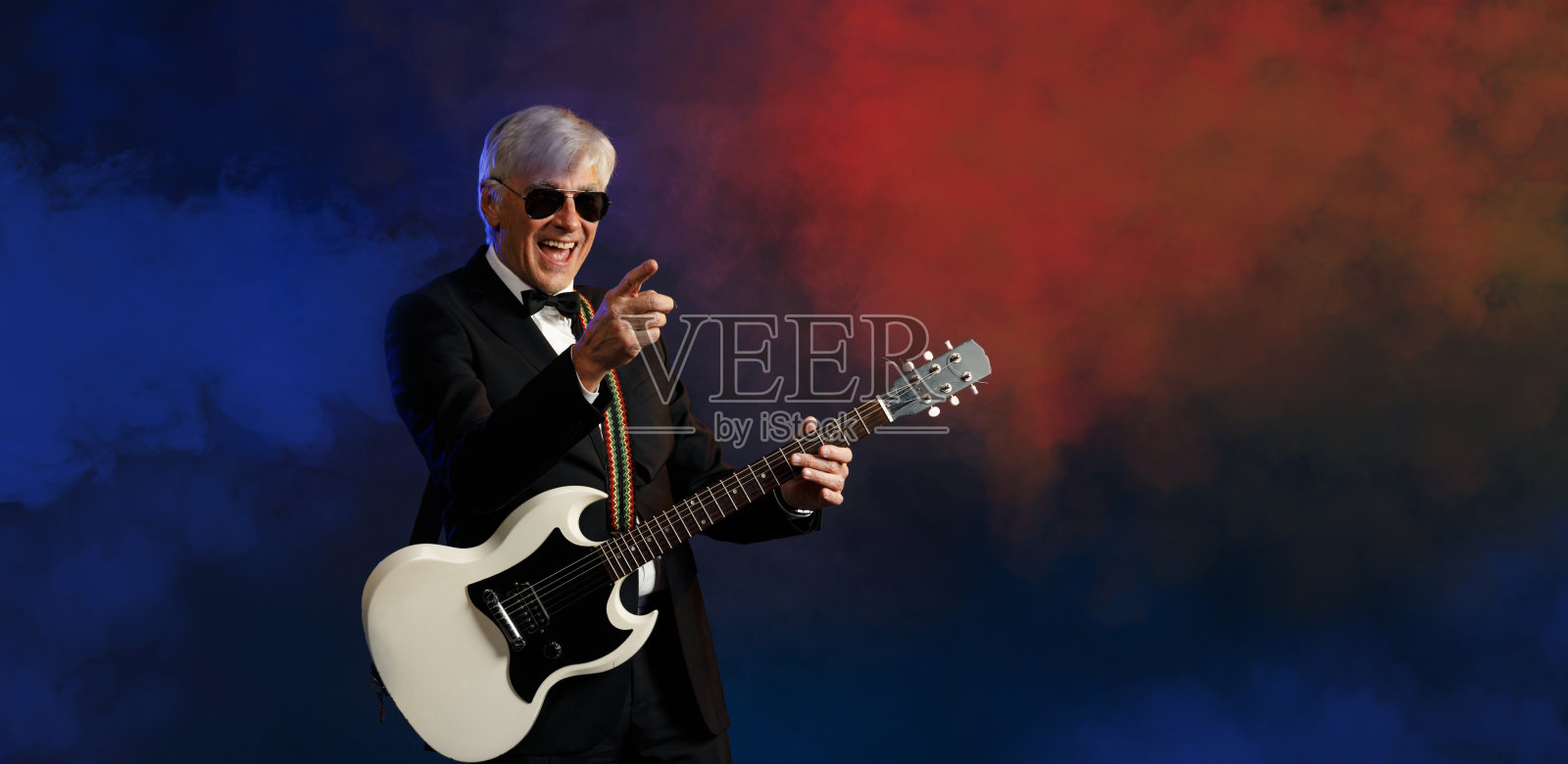 音乐家吉他手活跃的高级英俊男子弹吉他。蓝色背景，光线和烟雾特效。照片摄影图片