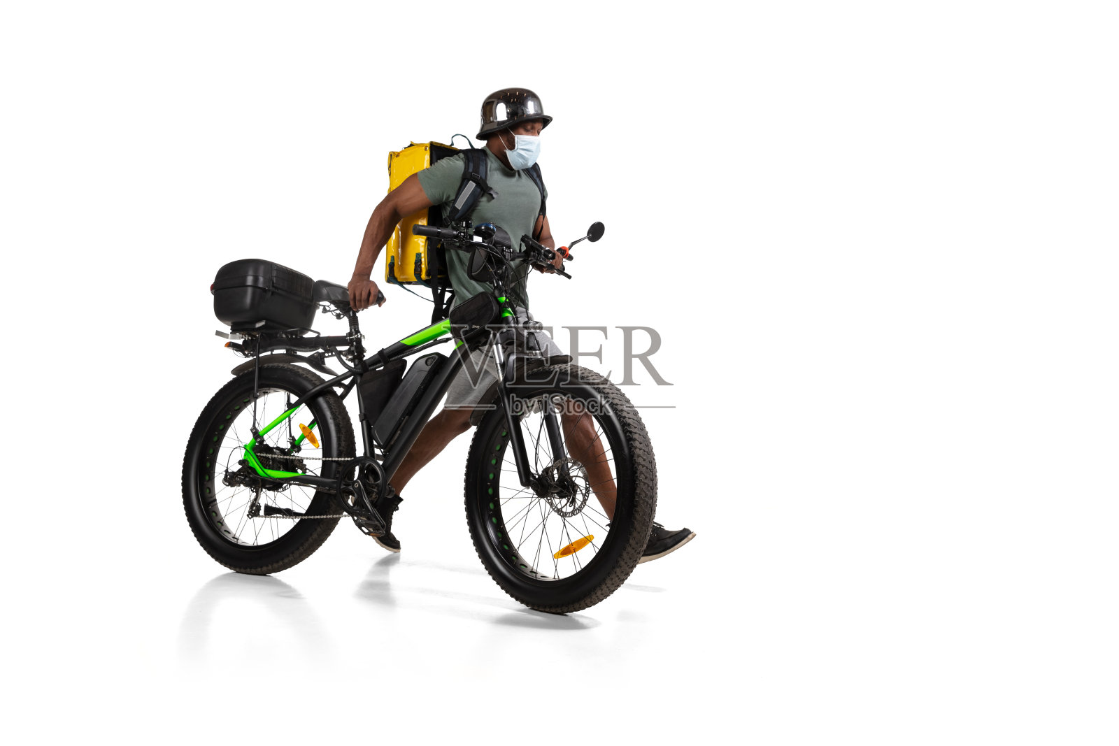 太多的订单。隔离期间的非接触交付服务。在隔离期间，男子戴着头盔和面罩运送食物和购物袋。照片摄影图片