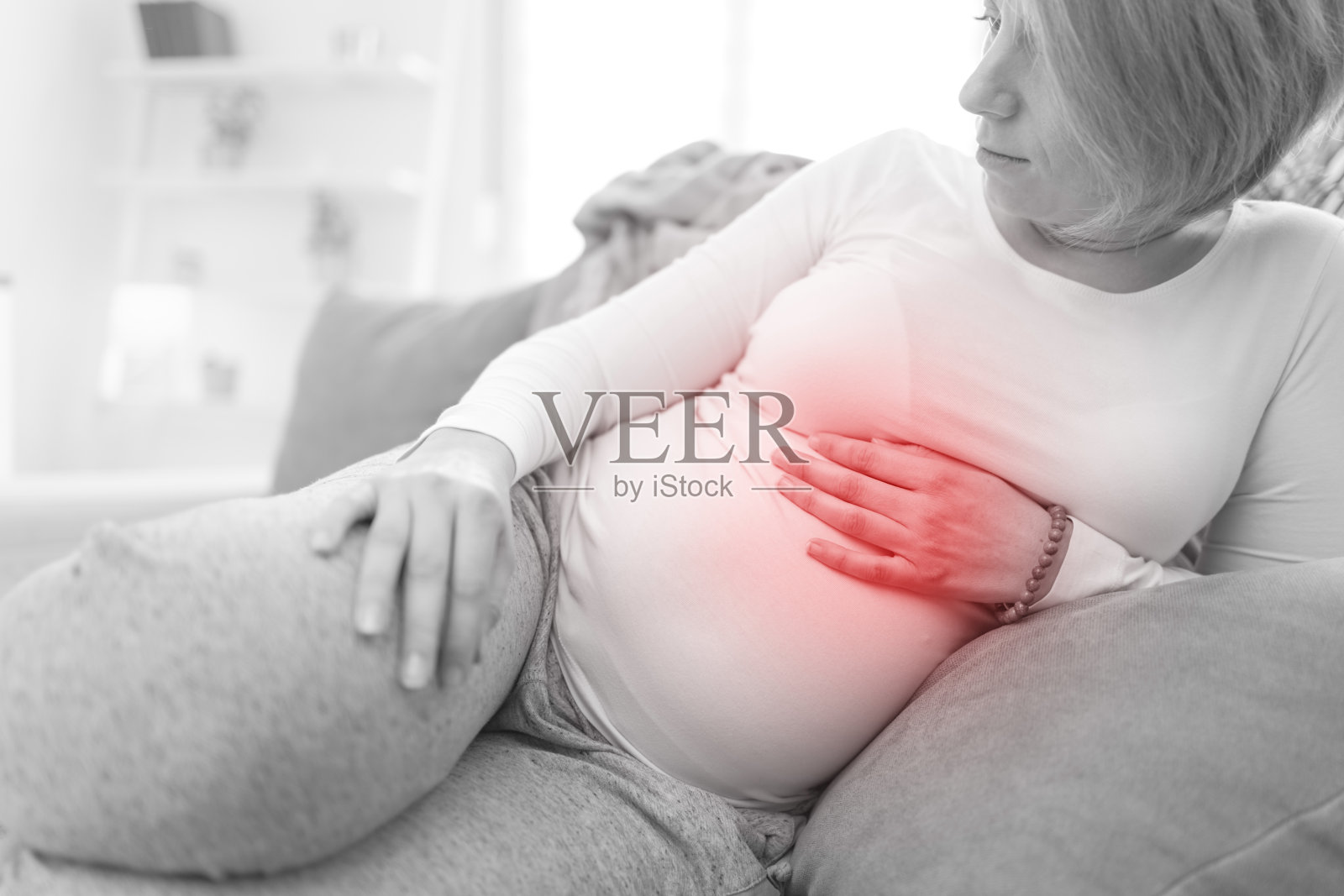 疲惫的孕妇在家中沙发上休息，有胃部不适。照片摄影图片