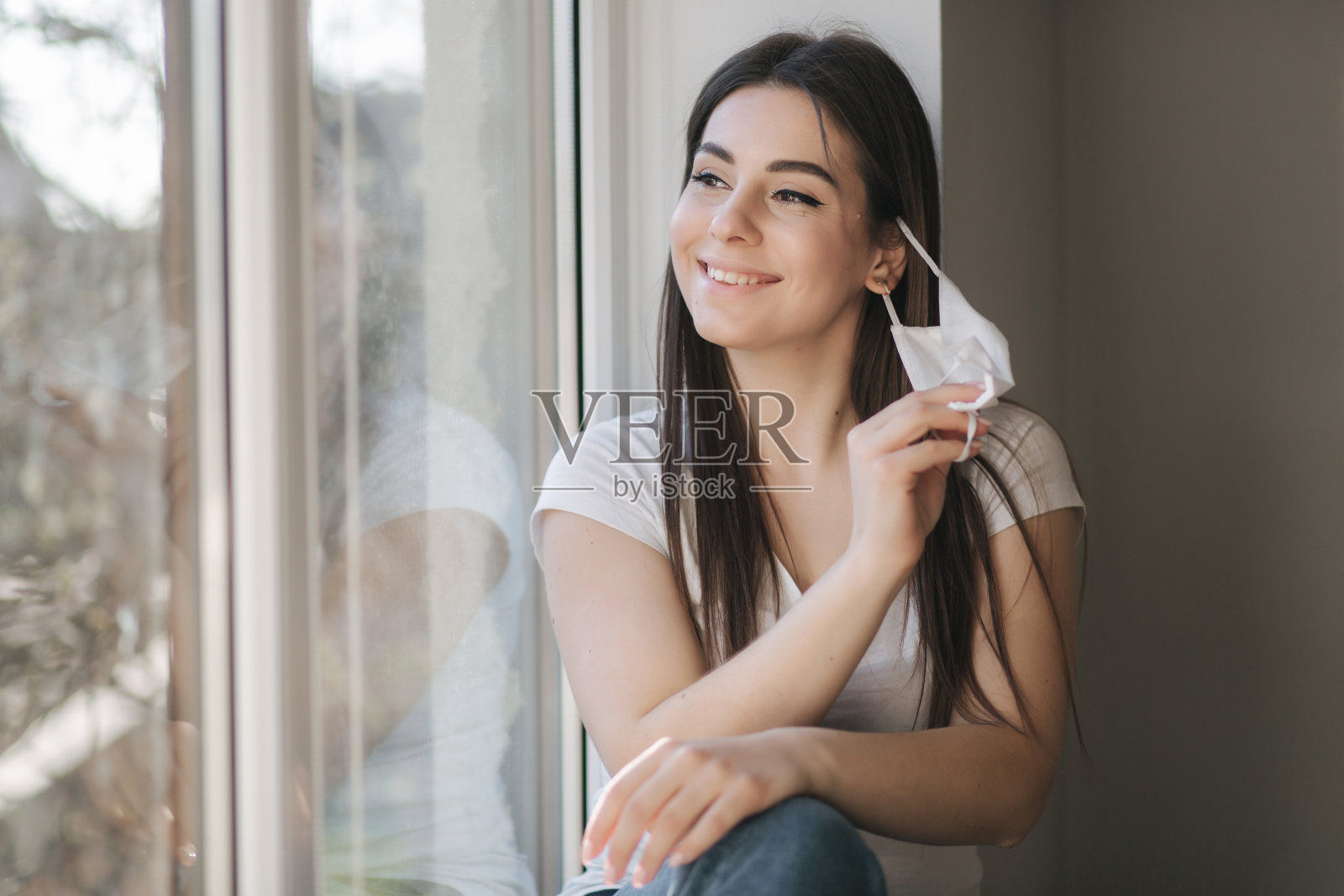 年轻女子摘下防护面具。穿着白色t恤和白色医用口罩的女性。检疫结束。冠状病毒的主题照片摄影图片