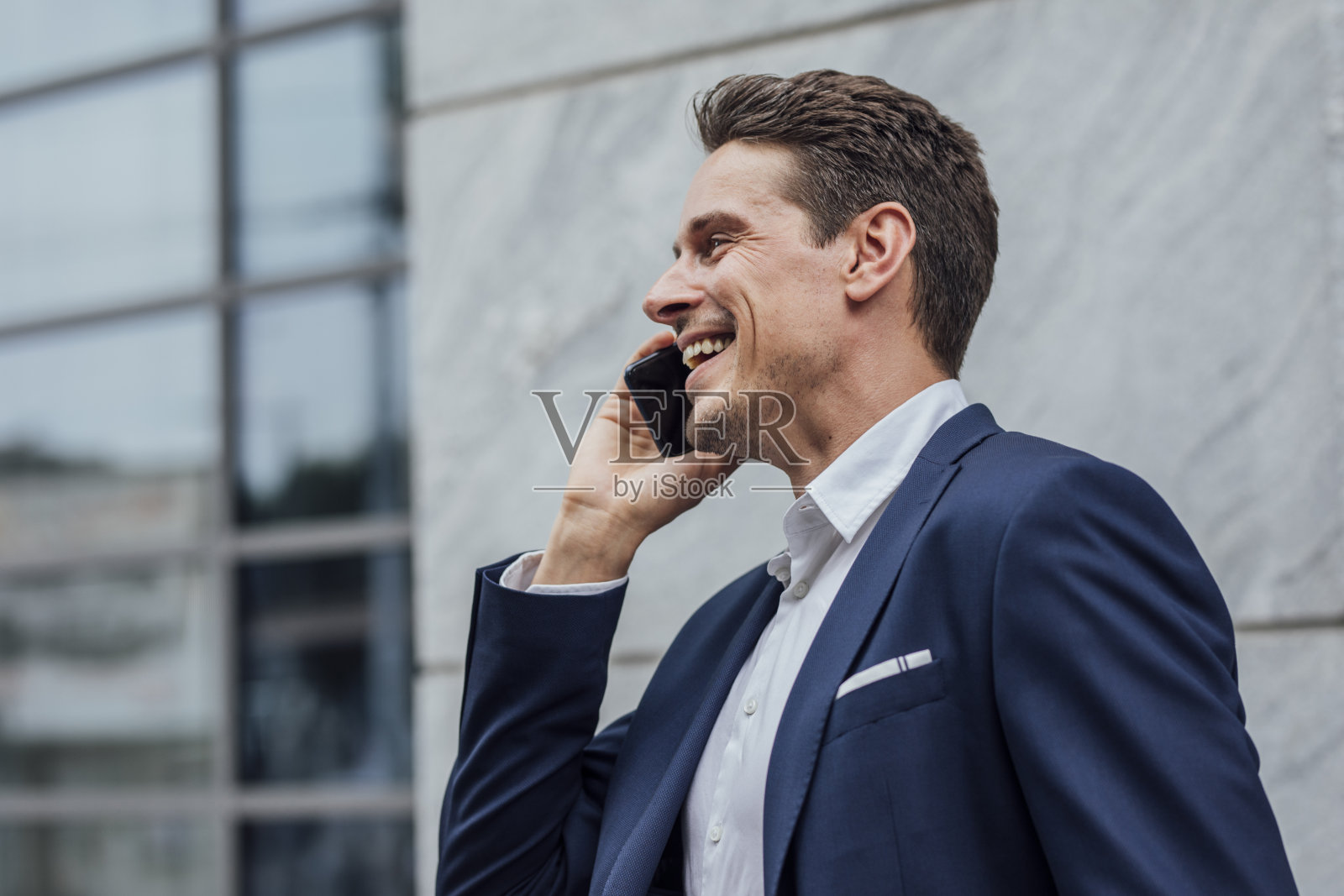 穿着蓝色西装的快乐英俊商人在街上打电话照片摄影图片