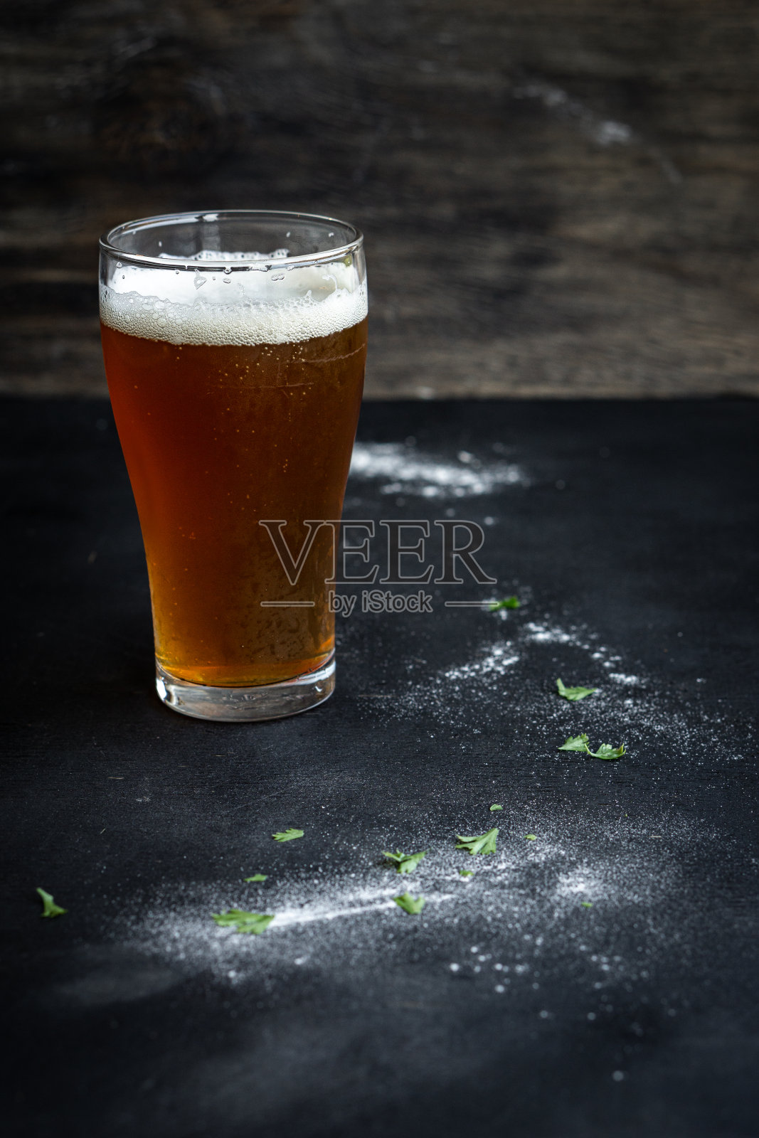 在木桌上烹饪时，用平底玻璃杯盛着清脆的淡啤酒。照片摄影图片