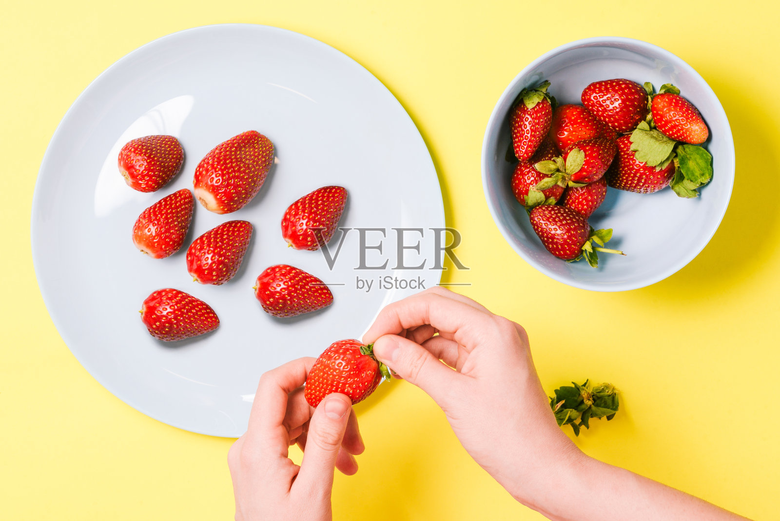 女孩剥草莓当早餐。男人的手拿着黄色背景上的草莓。健康和有益健康的食物。照片摄影图片