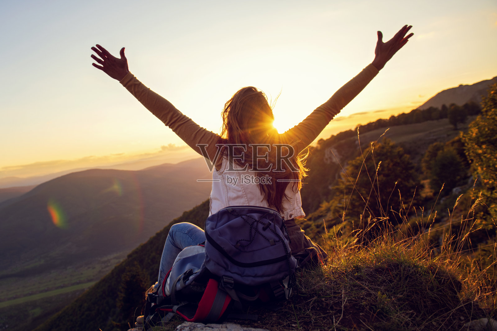 年轻女子在山顶和日落天空的抽象背景上举起手来。照片摄影图片
