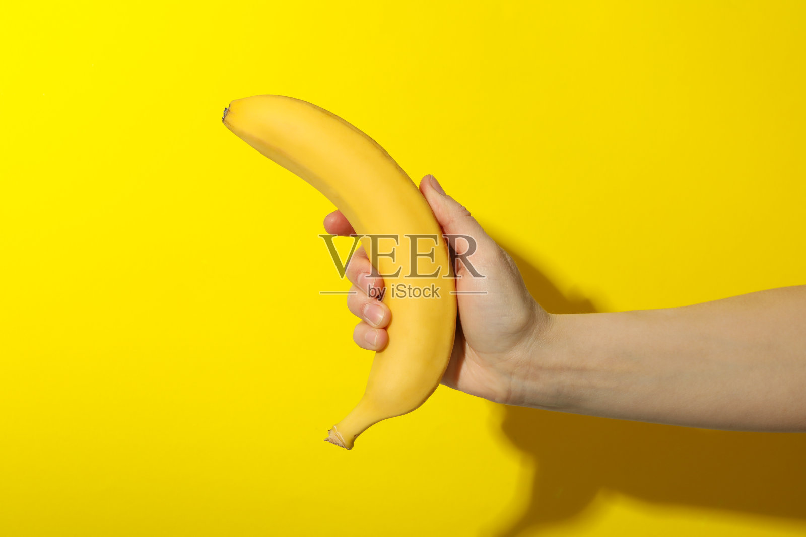 黄色背景上，女性手握香蕉。新鲜的水果照片摄影图片