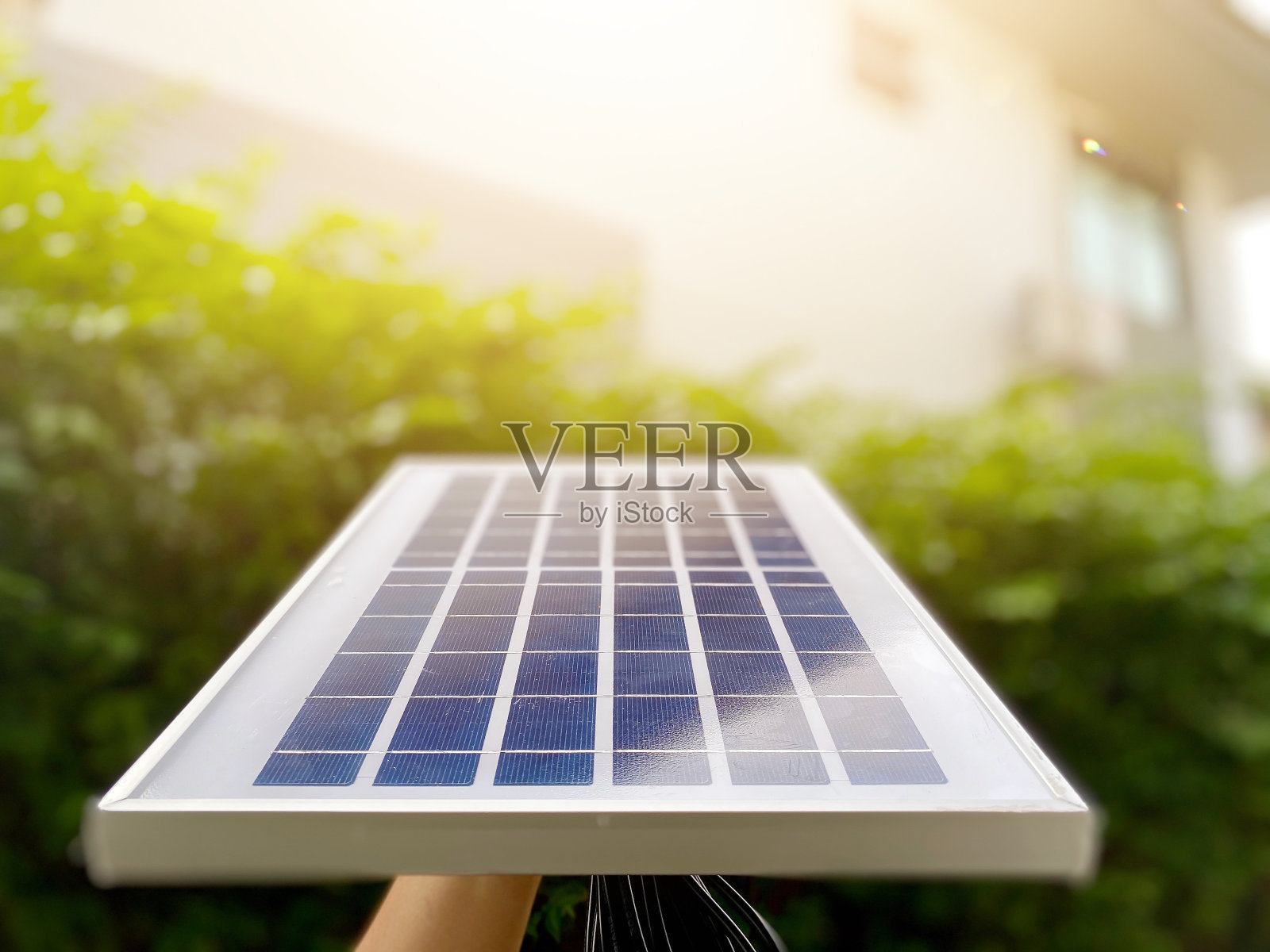 在有阳光的房子里，男人的手拿着太阳能板。可持续资源和减少电费的概念照片摄影图片