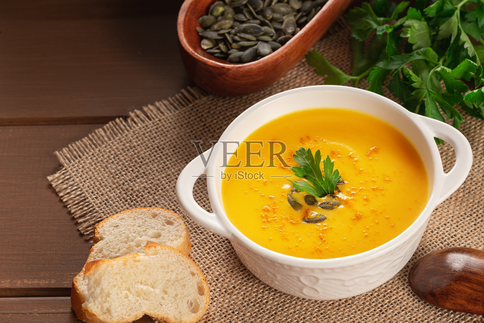 质朴的木桌上放着南瓜汤和欧芹。秋季时令食物-辣南瓜和胡萝卜汤。照片摄影图片