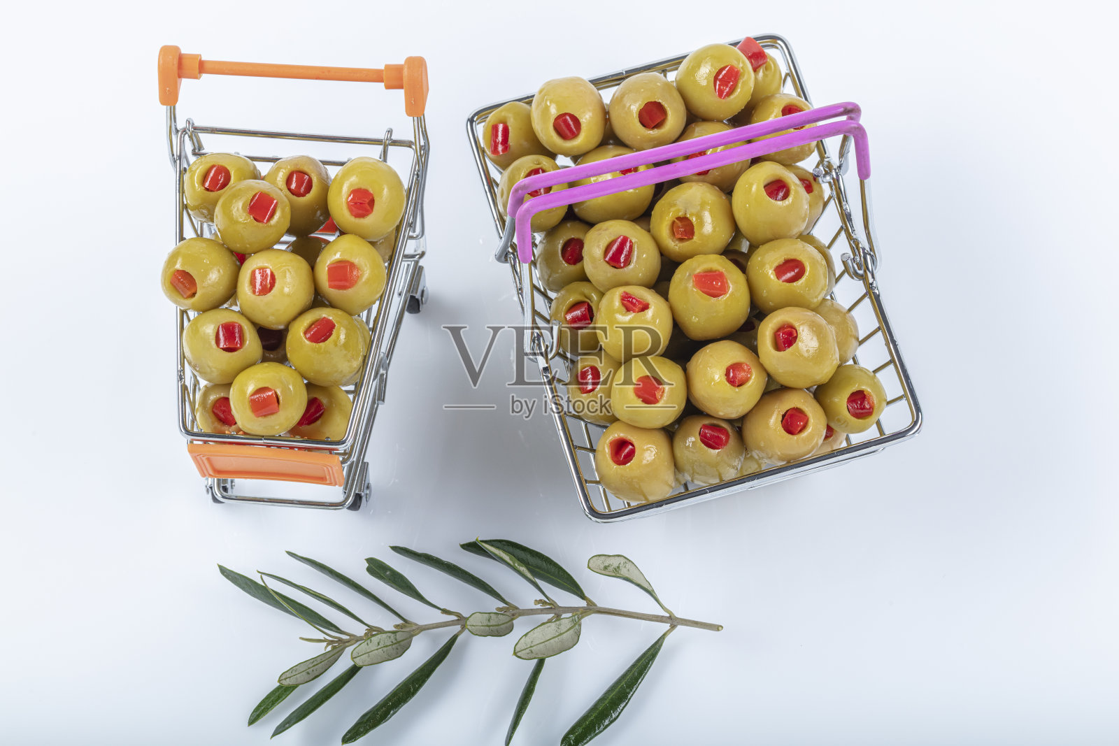 白色背景下的购物车里，塞满红辣椒的绿橄榄旁边是橄榄油和橄榄枝。照片摄影图片