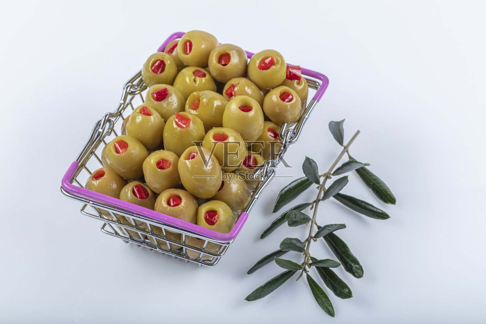 白色背景下的购物车里，塞满红辣椒的绿橄榄旁边是橄榄油和橄榄枝。照片摄影图片