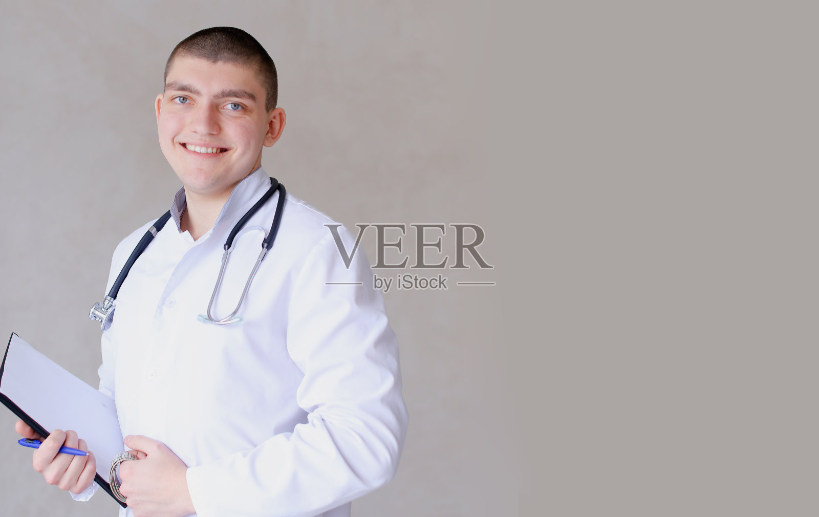 孤立的年轻医生站在文件和听诊器在灰色背景和副本空间照片摄影图片