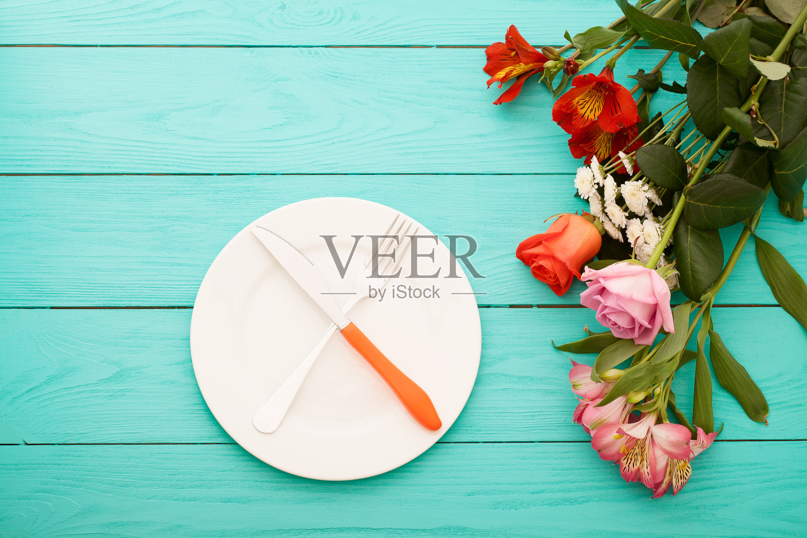 节日晚餐用刀叉盘子和玫瑰在蓝色的木制背景。前视图。模拟。花。本空间照片摄影图片