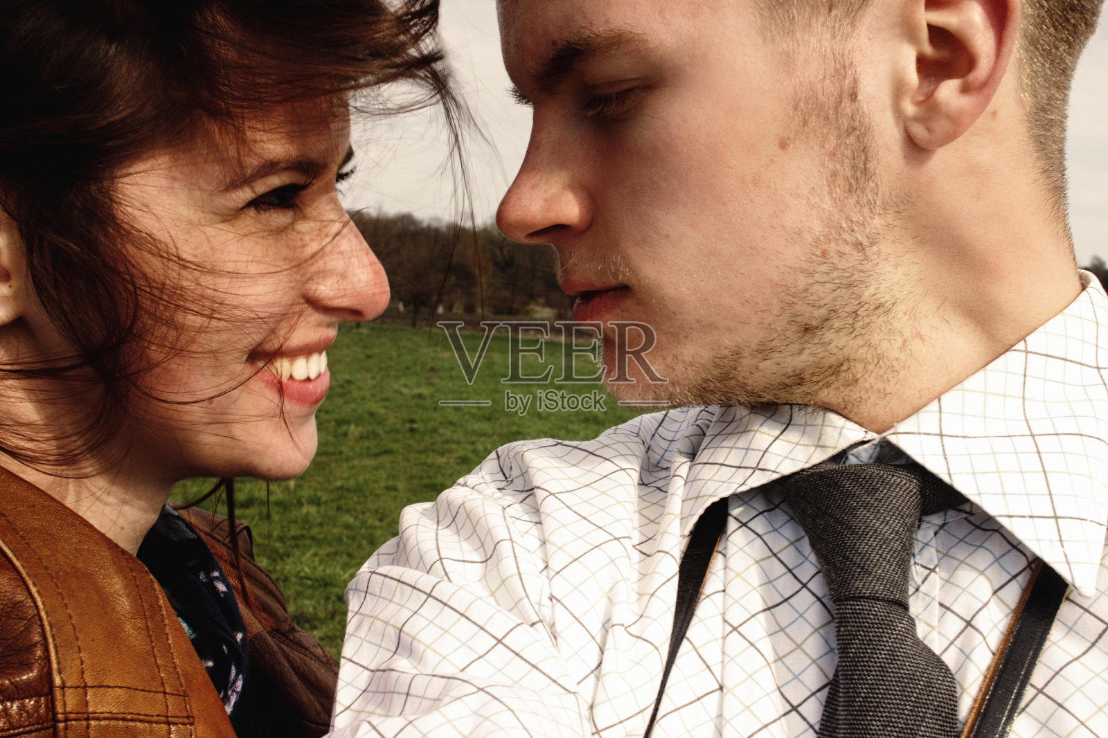 时尚的黑发美丽的女人和男人在有乐趣和微笑在多风的春天的田野照片摄影图片