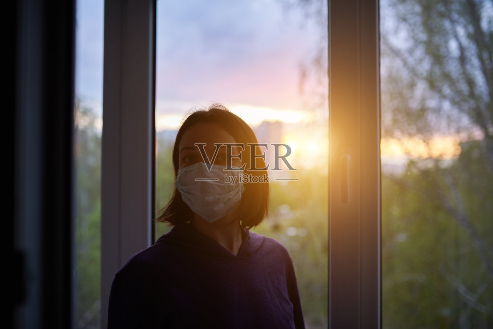 因病毒爆发在家中被隔离的日落窗口附近的妇女。呆在家里的概念照片摄影图片