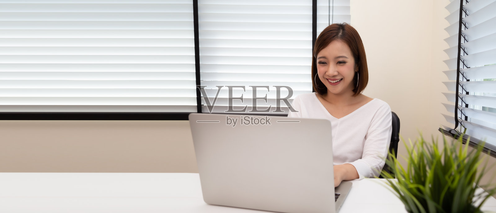 年轻的亚洲女性工作与笔记本电脑在她的公寓的白色书桌上，在家工作的概念照片摄影图片