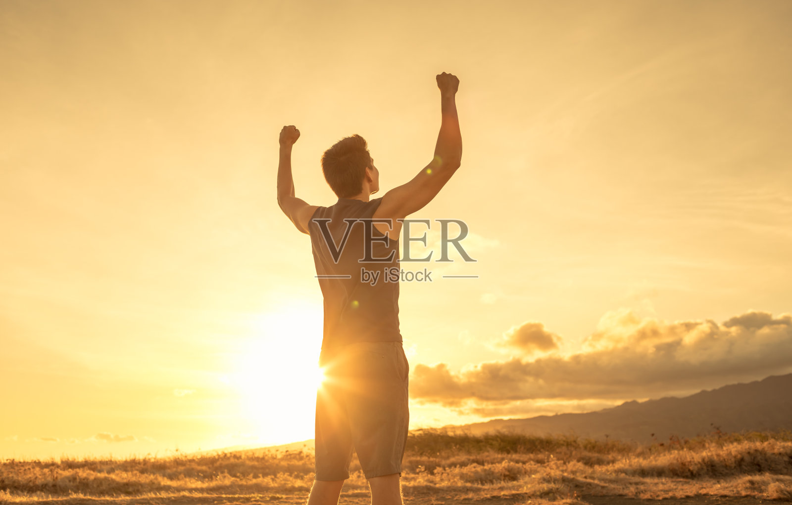 强壮强壮的年轻人举起拳头，望着夕阳下的天空。照片摄影图片