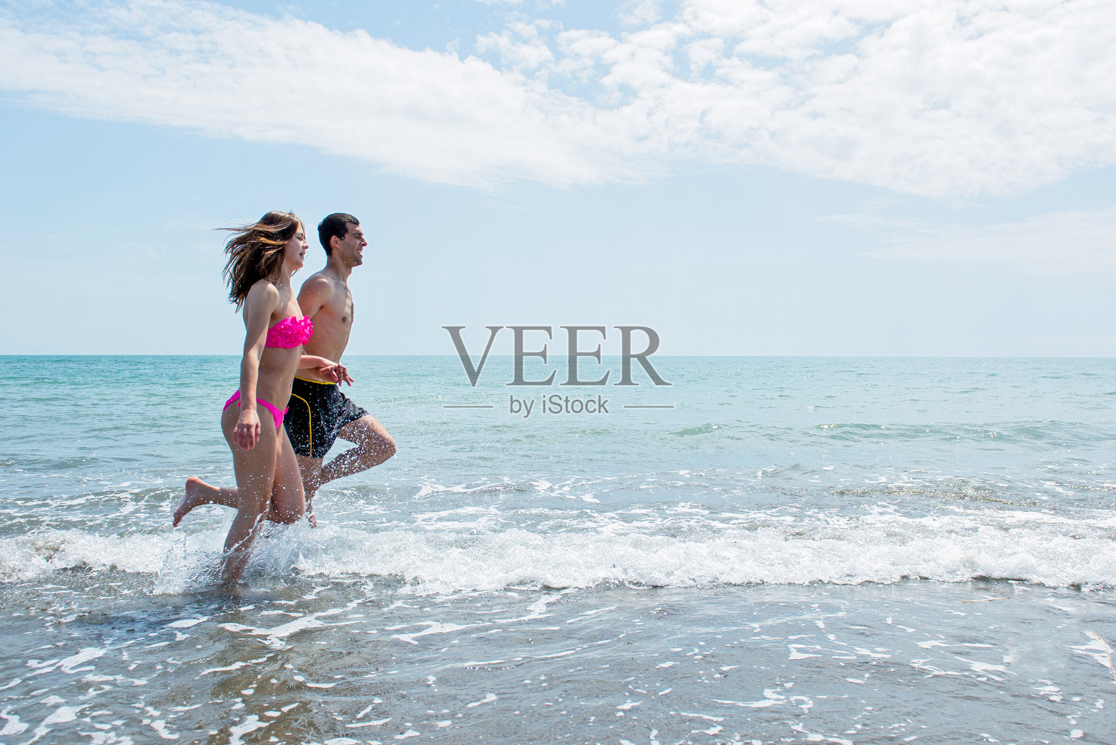 快乐的年轻夫妇在阳光明媚的一天在海滩玩照片摄影图片