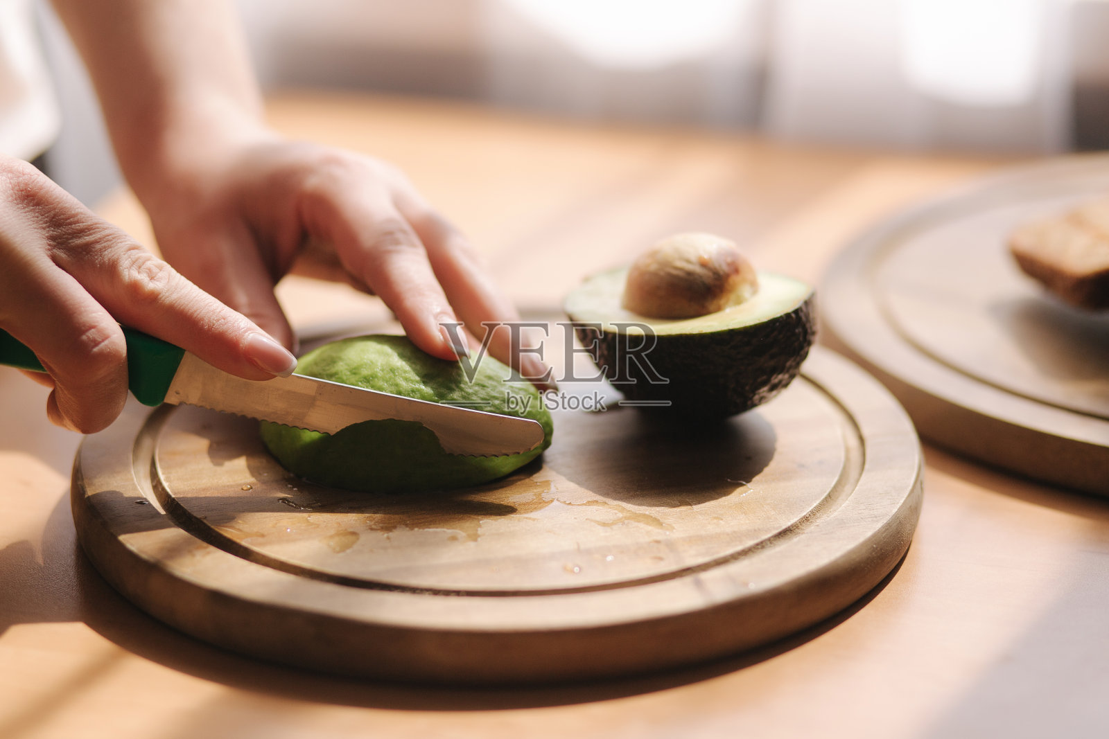女人在家里的木板上切牛油果的特写。素食的概念照片摄影图片