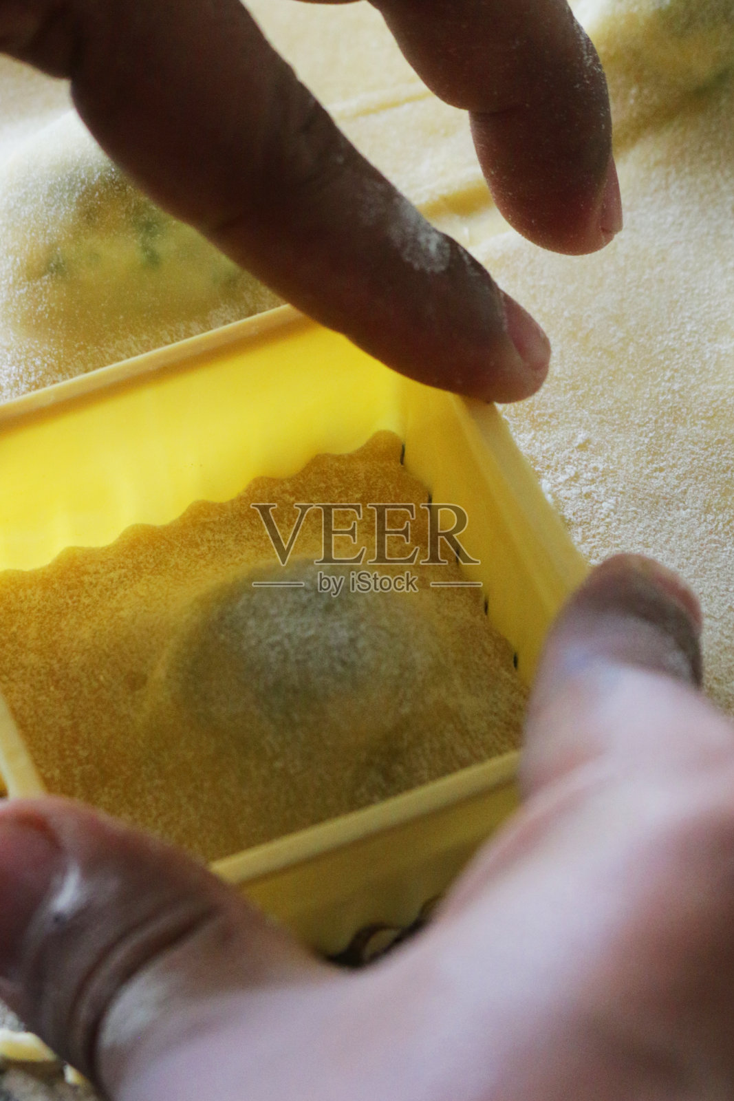 一个不认识的人用方形的糕点切割器把填满菠菜和乳清干酪球的面皮做成自制的意大利饺子照片摄影图片
