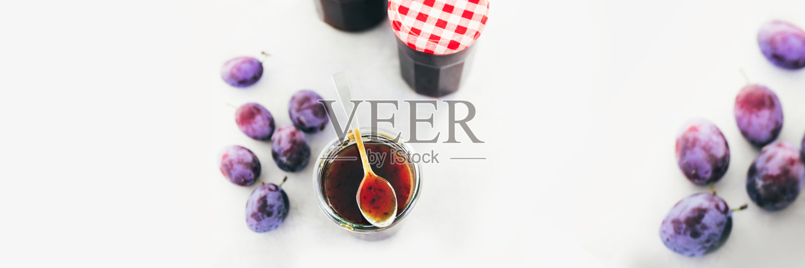 玻璃罐里的李子酱，散落着成熟的李子。照片摄影图片