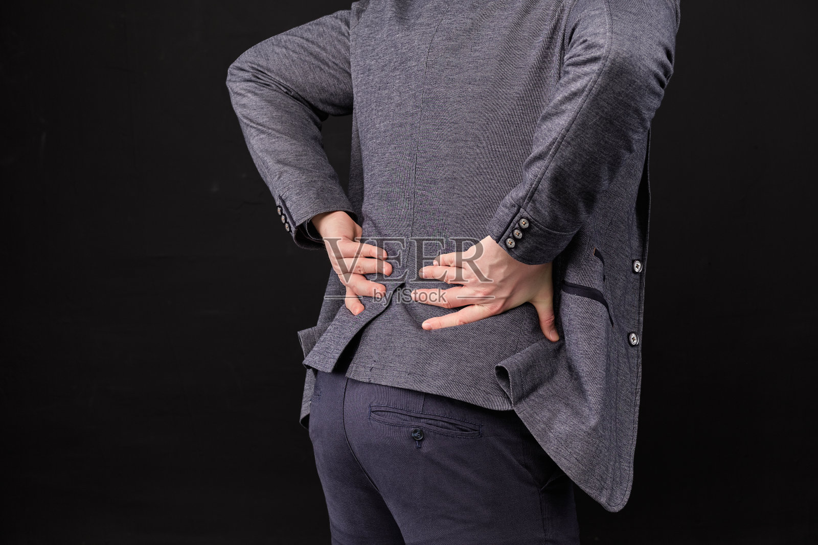 一个穿着夹克的男人用他的手在黑色的背景上按摩下背部。照片摄影图片